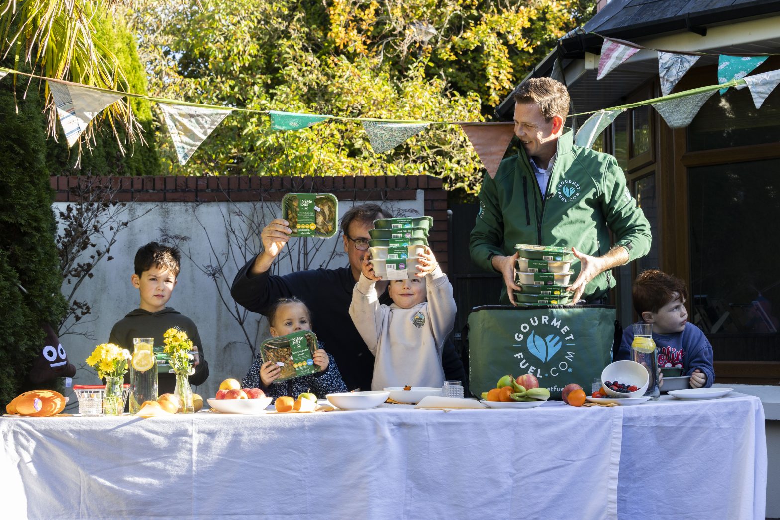 Adults and children sitting and standing at a table outdoors holding food products